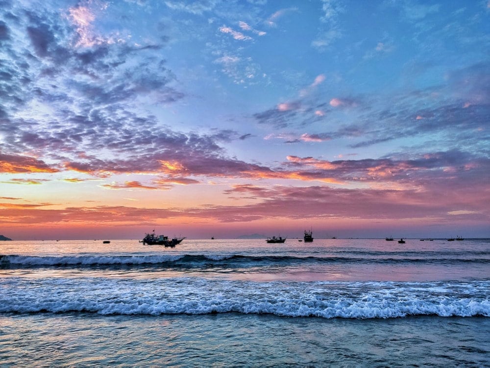 As the sun sets, fishing boats slowly make their way back to shore after a long day out at sea